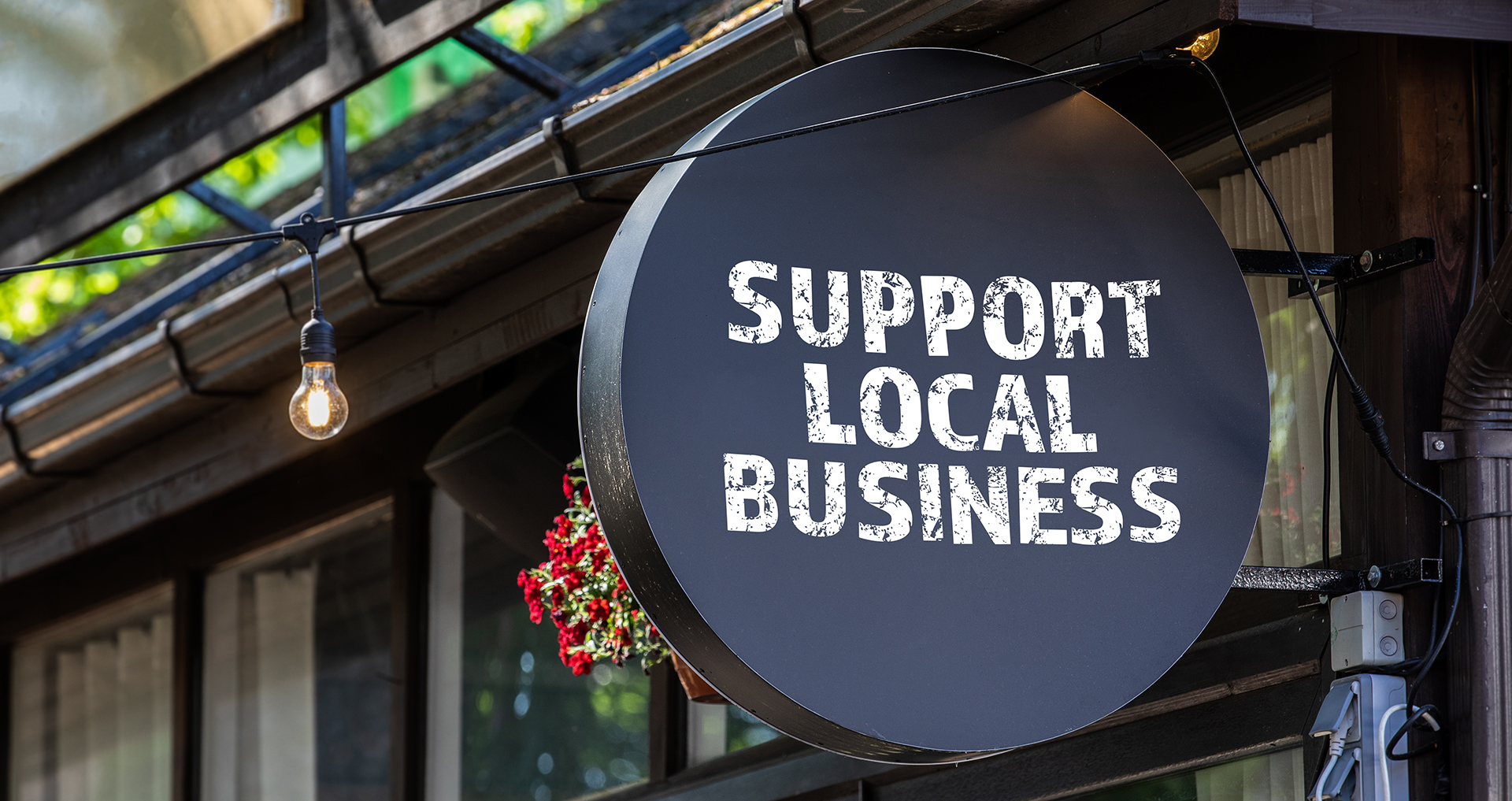 Support local business. Round, black sign onn teh wall of the house.